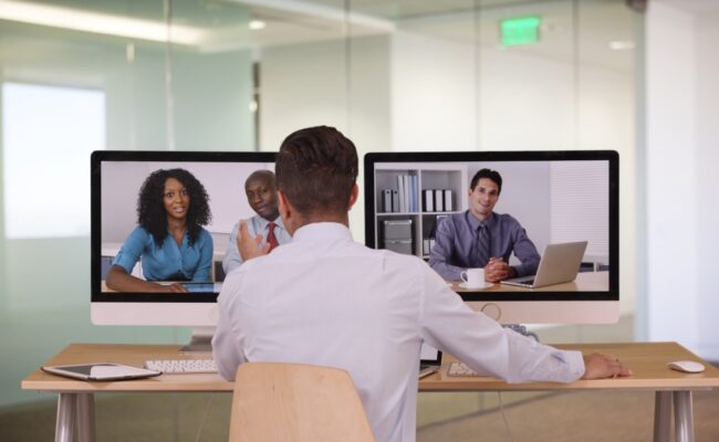 a man sitting at a desk while on a video call with coworkers