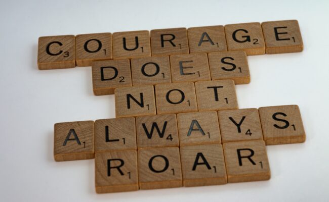 scrabble board game pieces spelling "Courage does not always roar"