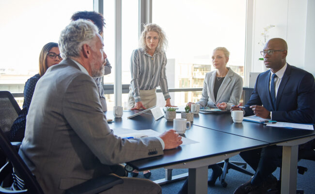 Mature manager talking to a diverse team of employees during a meeting around a table in a modern boardroom